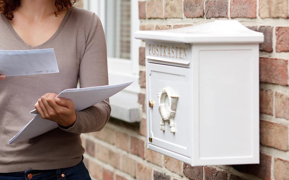 Frau holt Post aus einem weißen Standbriefkasten aus Guss